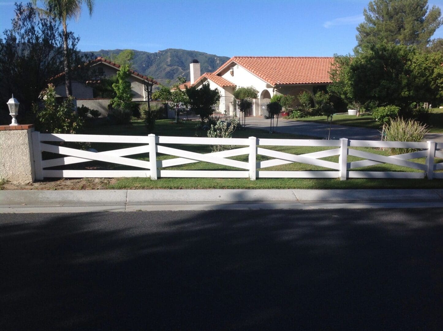 Suburban house with white fence and trees.