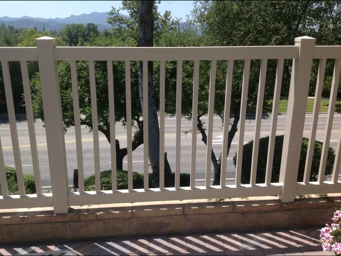 Fence overlooking road with trees and mountains.