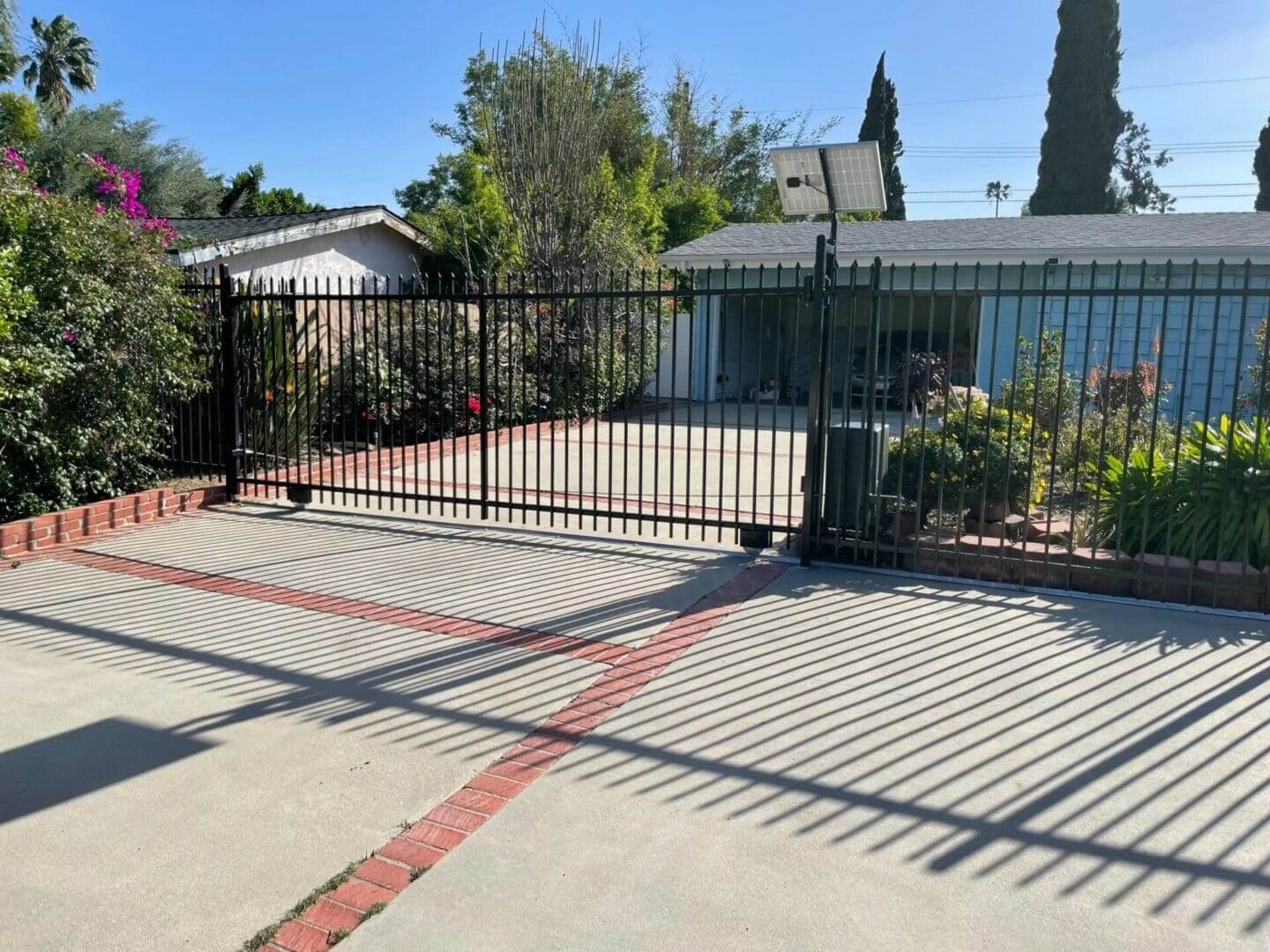 Driveway with metal gate and greenery.