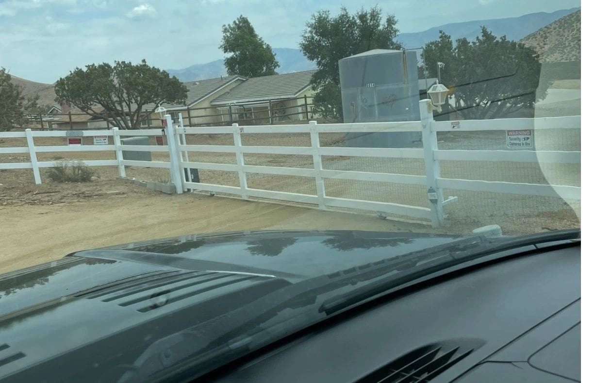 Car approaching white fence gate, rural setting.