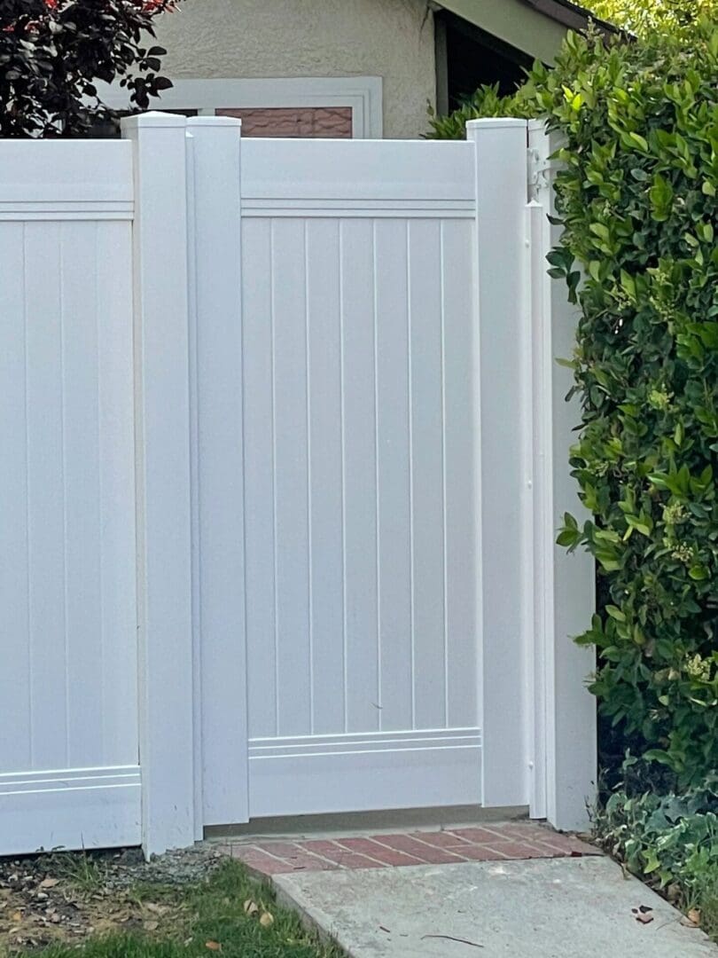 White fence gate beside green hedge.