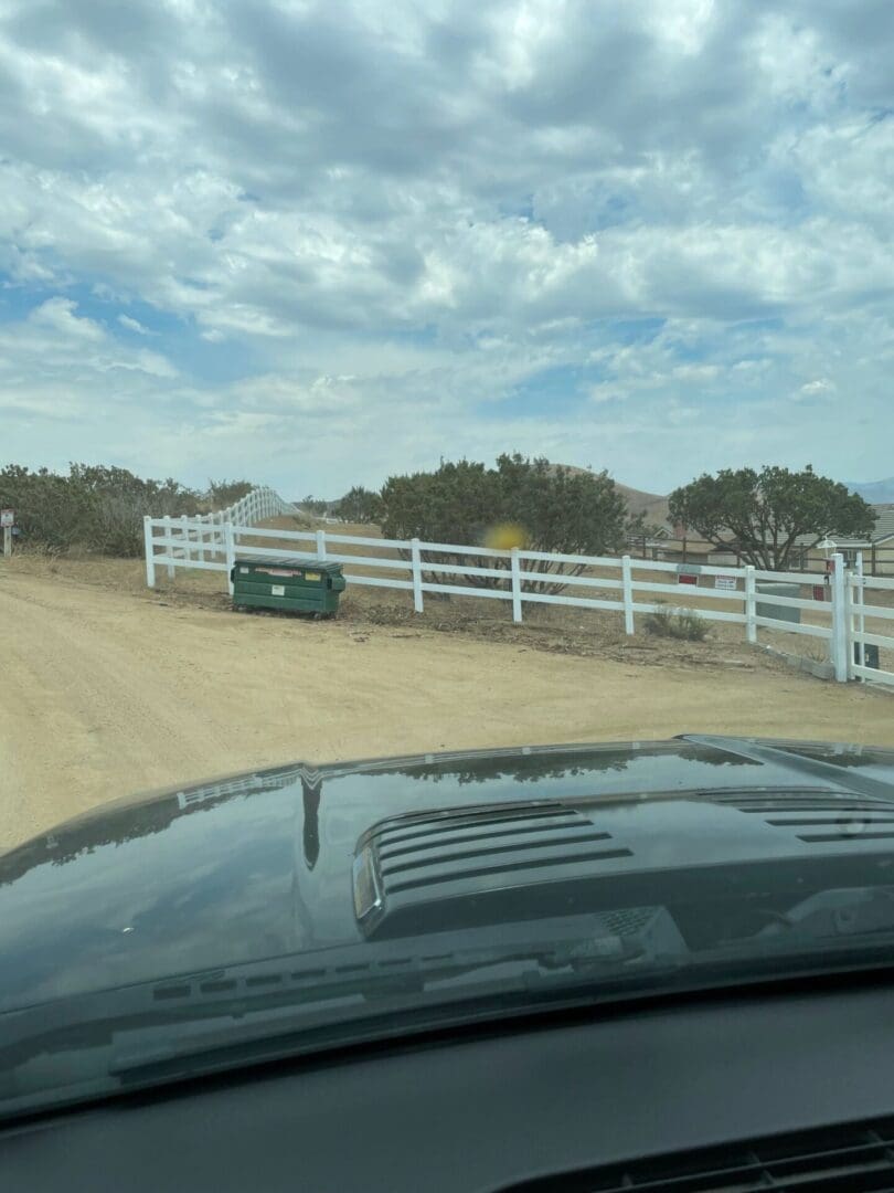 Car on dirt road near white fence.
